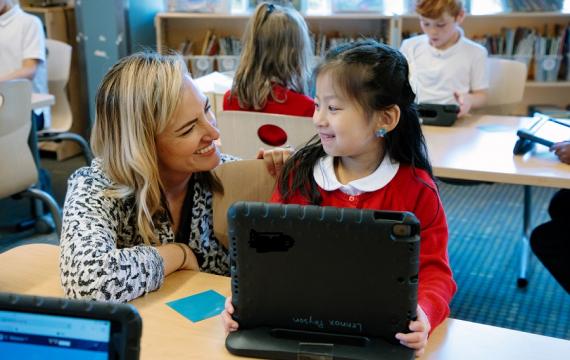 Young student at the Ephiphany school works on a laptop and is helped by her math teacher