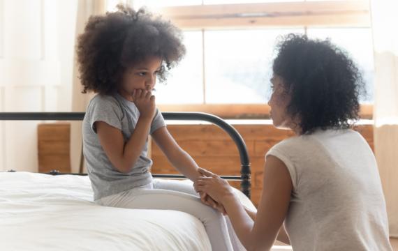 Young girl looking shy and sitting on a bed holding hands with a mother