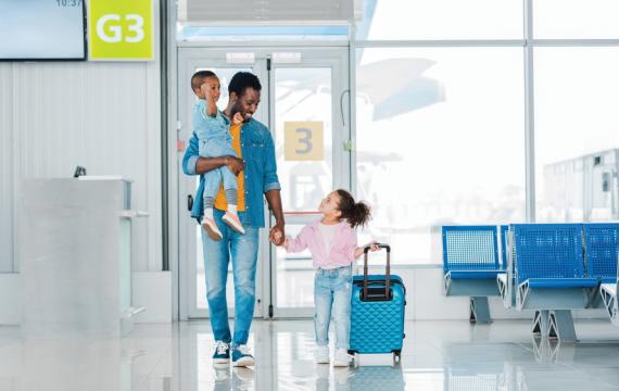Father carrying baby and  holding hand of a young girl pulling a suitcase in an airport