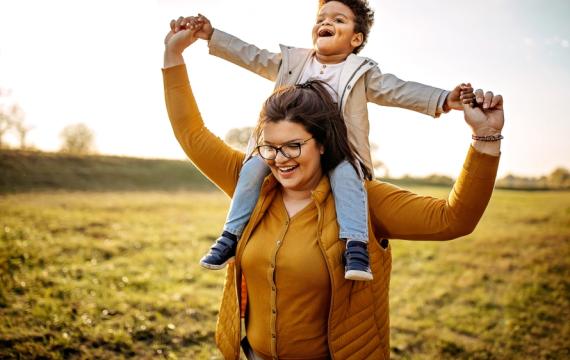 Woman with child on shoulders walking in a field