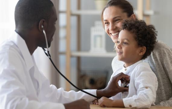 Doctor examining a young boy who is smiling and sitting on his mother's lap