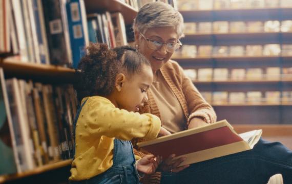 Grandma and child sitting on the floor of a library reading a book 