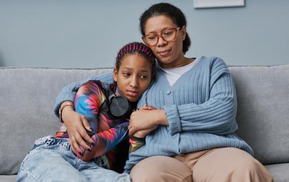 Woman hugging a tween girl sitting on a couch