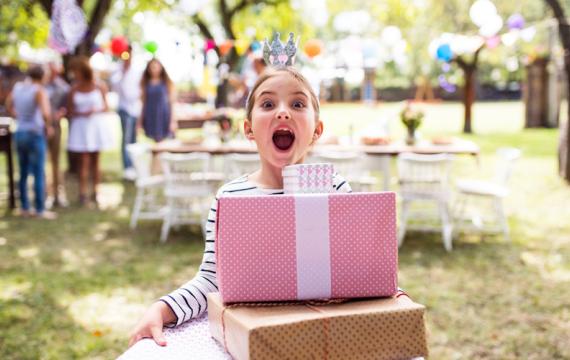 Young girl holding a stack of packages at a birthday party in a park, an easy outdoor birthday party idea for kids
