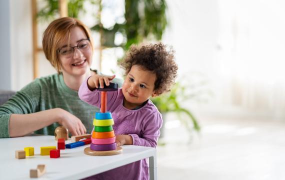 Nanny looking at a child who is playing with an educational didactic toy
