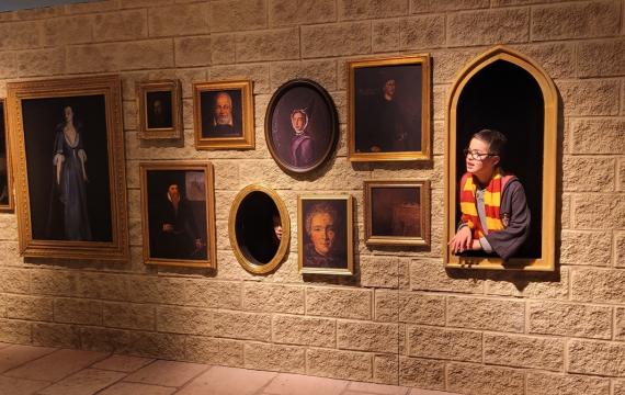 A boy peers out of an empty picture frame on the wall at Harry Potter: Magic at Play Harry Potter experience in Seattle Bellevue