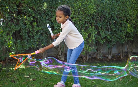 Girl blowing bubbles in the back yard spring break at home