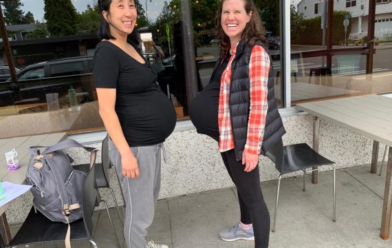 Pregnant mom friends face each other smiling. 