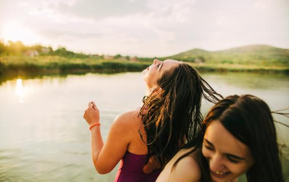 two teens laugh by a lake at dusk