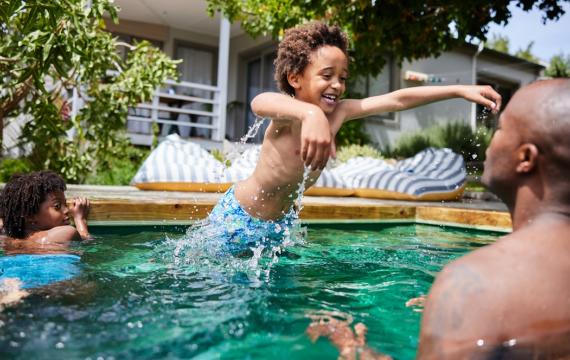 Boy jumping in his father in a swimming pool and demonstrating water safety for families 