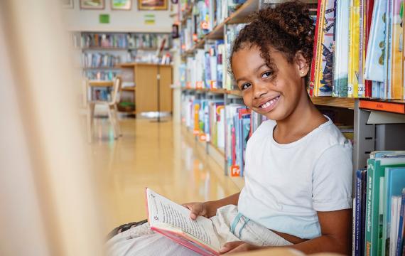 little girl sitting in the library reading a book