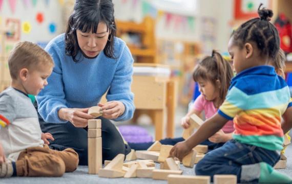 A teacher with kids in a day care playing with blocks 