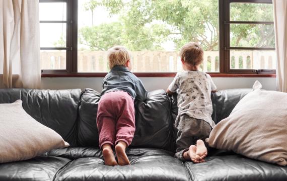 two kids sitting on a couch looking outside