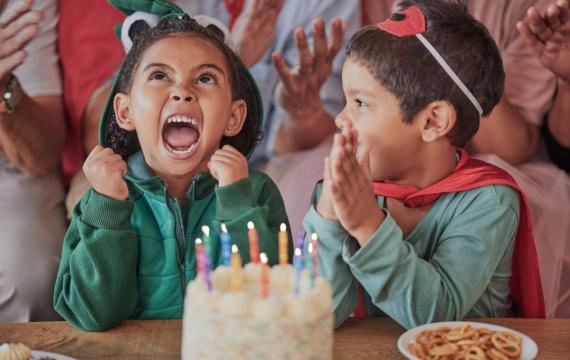 An excited child wearing a costume sits in front of cake at a toddler birthday