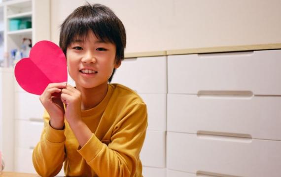 A boy holds a red heart while making crafts for Valentine's Day.