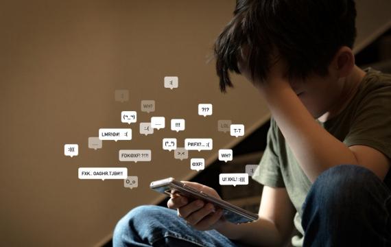 preteen boy covering his face with hands holding smartphone in low light