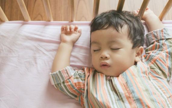 Little boy toddler adorably sleeping in his baby cot