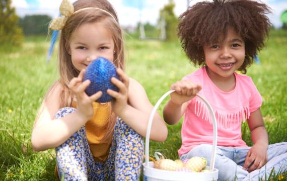 Two girls sitting on grass, holding eggs and basket for Easter.