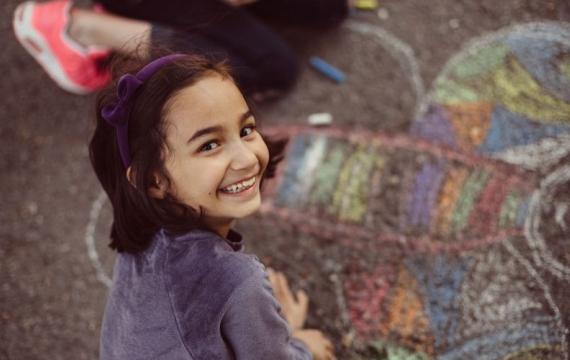 A young girl creates chalk art on the sidewalk.