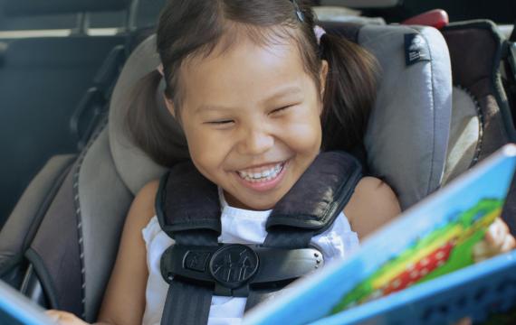 girl in a car seat with a fun car toy happy on a road trip