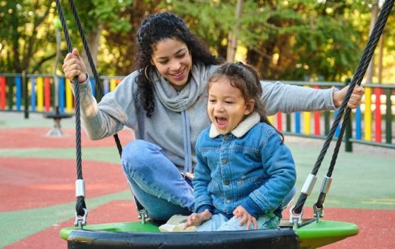 mom playing with child on swing at playground