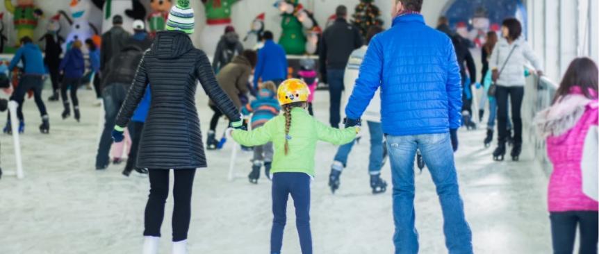 Two parents and a girl, seen from the back, ice skate at Bellevue Downtown Ice Rink a seasonal outdoor covered skating rink near Seattle Washington