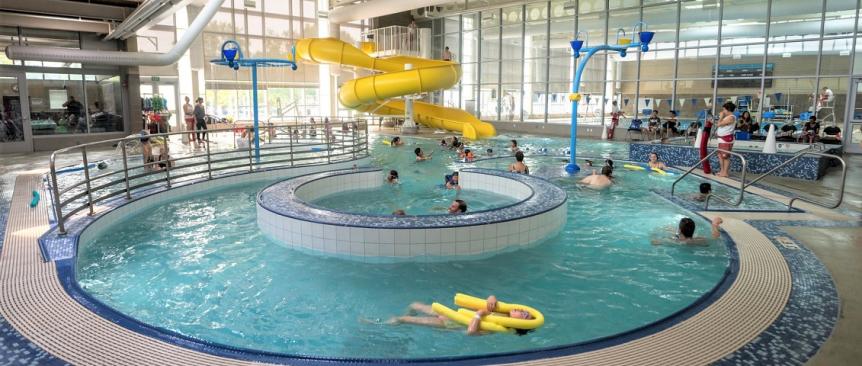 View of people swimming in Rainier Beach Pool in Seattle. Yellow twister slide is in the backgorund and the lazy river feature is in the foreground