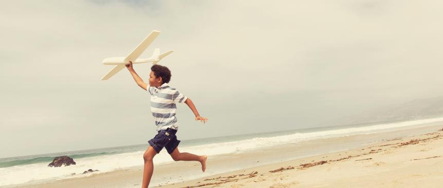 Young boy races down a beach preparing to launch a model glider