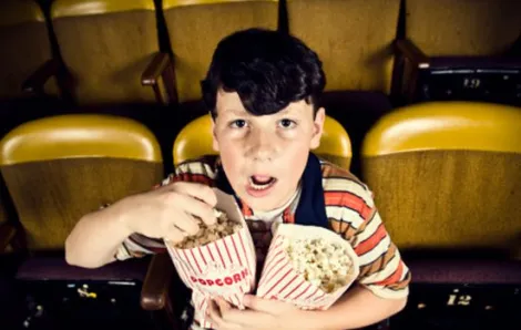 Boy watching a movie and holding two bags of popcorn