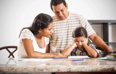 Young girl doing homework with her parents