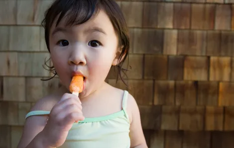 Girl eating popsicle after playing indoors when it's too hot to play inside
