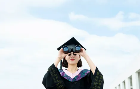Young woman graduate looking through binoculars 