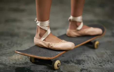 A girl in ballet shoes riding a skateboard