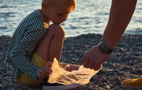 A young boy helps his father collect garbage on the beach at sunset 