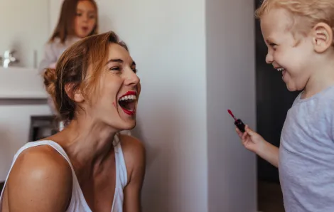 Mom laughs as her child puts lipstick on her face