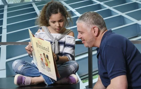 Young girl reads a book to her father at the Seattle Public Library Central Branch