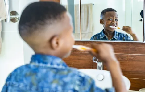 little boy brushing his teeth in the mirror