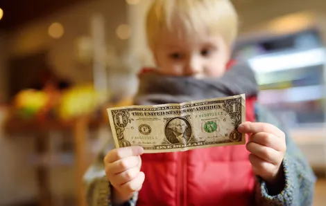 little boy wearing a red jacket holding a dollar bill
