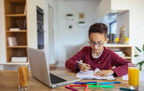 kid sitting at a table with a computer and papers doing online learning