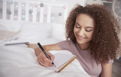 teen girl writing in a notebook on her bed