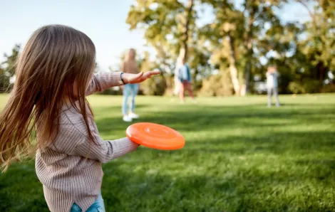 girl-playing-frisbee-with-family-in-park-on-sunny-day-safety-tips-going-outside-coronavirus