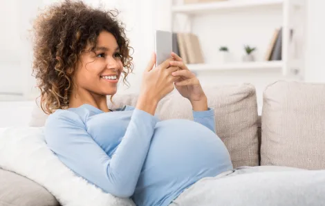 pregnant woman on the couch looking at her cell phone smiling