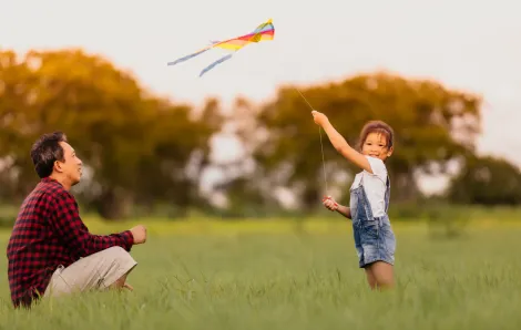 dad and daughter flying a kite in a field 