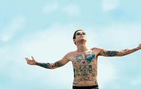 the king of staten island cover photo with tattooed pete davidson standing with his arms out