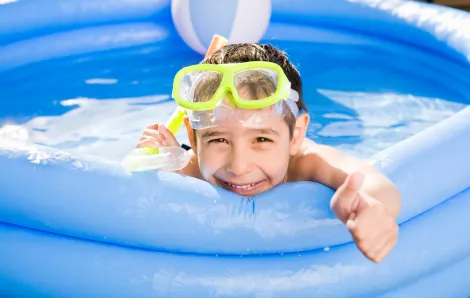 little boy wearing a snorkel in a pool in the backyard smiling at the camera