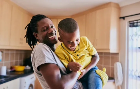 smiling black dad wearing rubber gloves and lifting up his laughing son 
