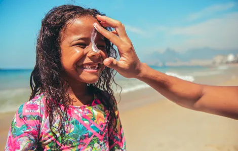 little smiling girl on the beach with her mom's hand swiping sunscreen down her nose