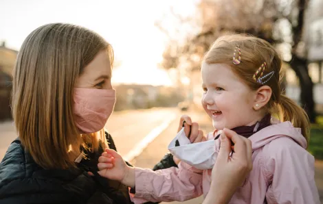 mom putting a mask on her smiling daughter