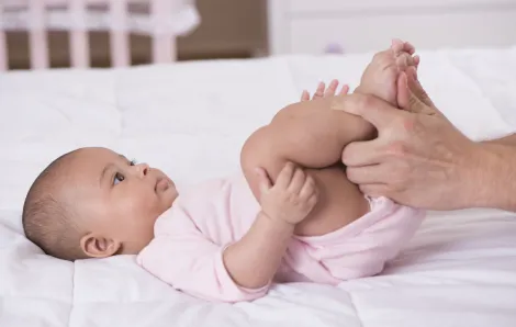 baby on her back looking at a parent with their hands on the baby's legs