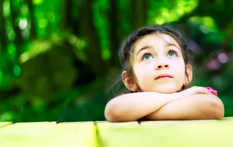 little girl outdoors leaning her crossed arms on a table looking up at the sky